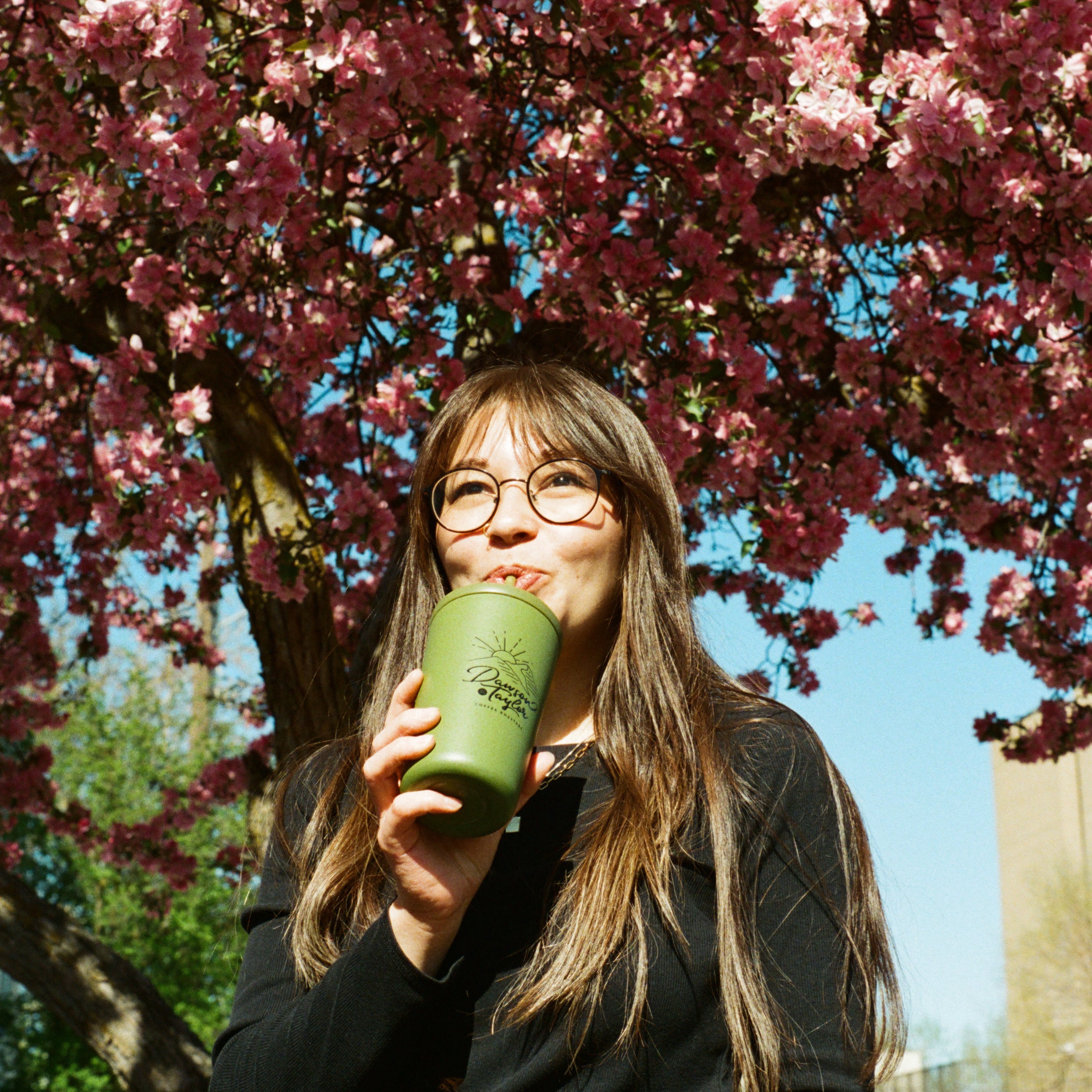 Person drinking from a green cup under a cherry blossom tree