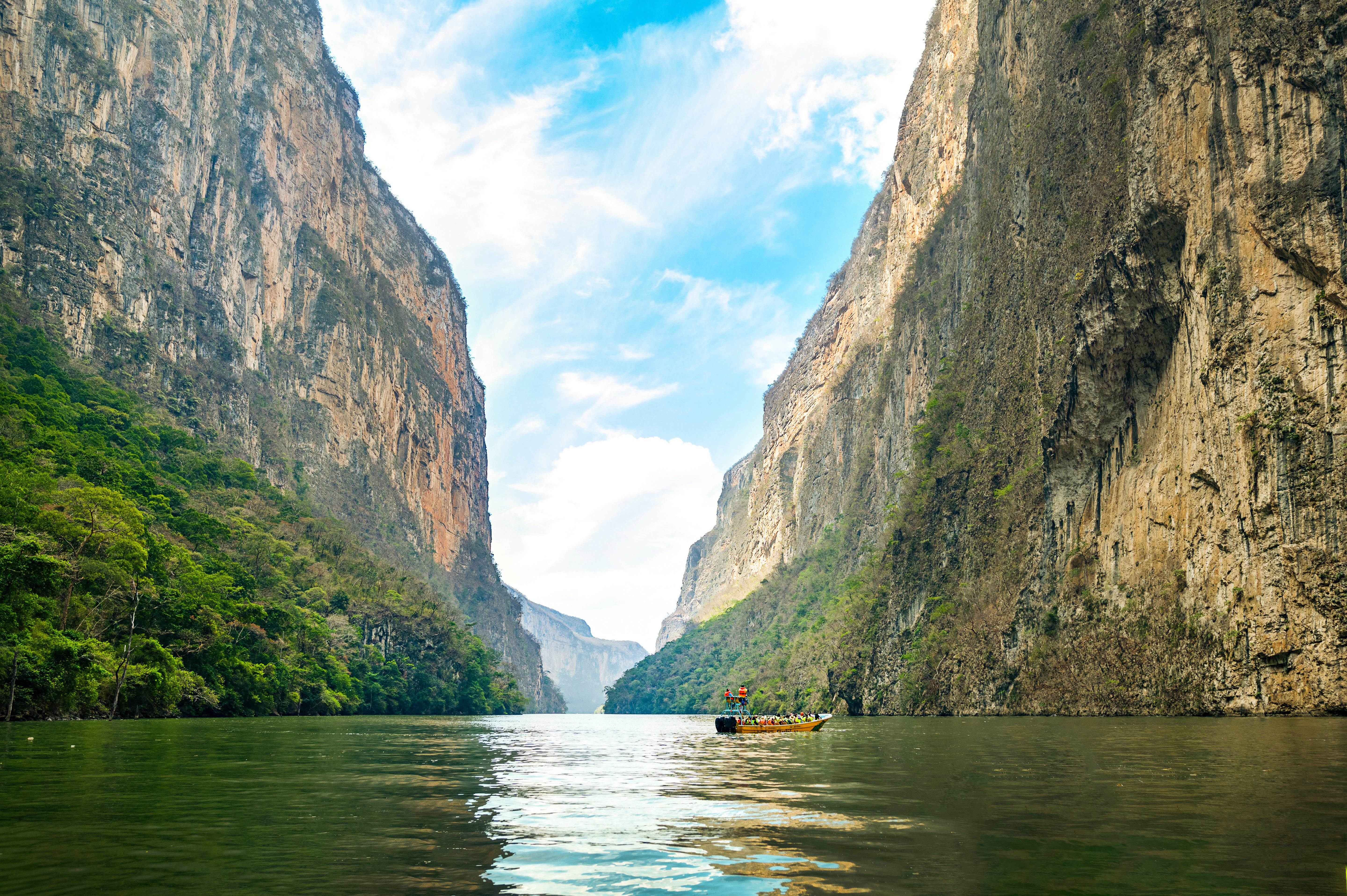 Boat navigating a narrow canyon between towering rock walls with a clear blue sky.